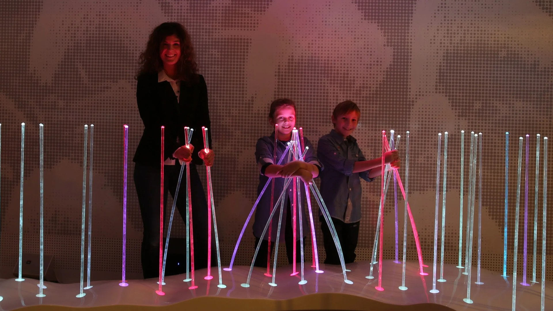 Visitors interacting with illuminated vertical rods in an Audioversum exhibit