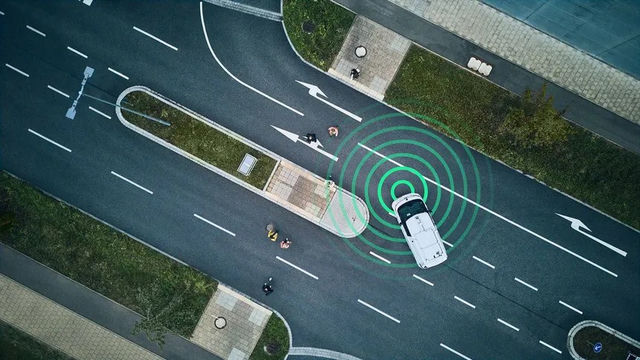 Overhead view of a car at a road junction with green sensor rings extending towards pedestrians