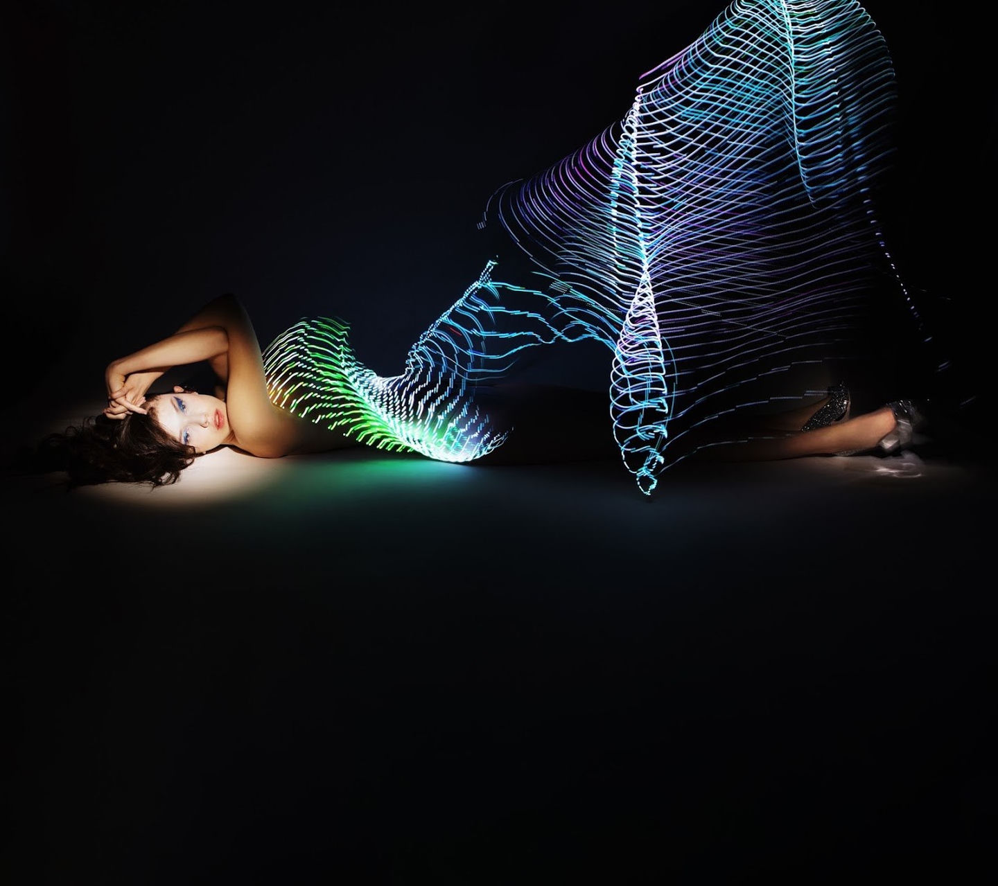A figure in a long-exposure fashion photograph surrounded by flowing multicoloured light trails
